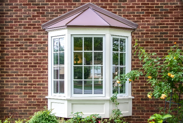 A set of bay windows looks out from a brick house with a metal roof keeping it safe and dry.