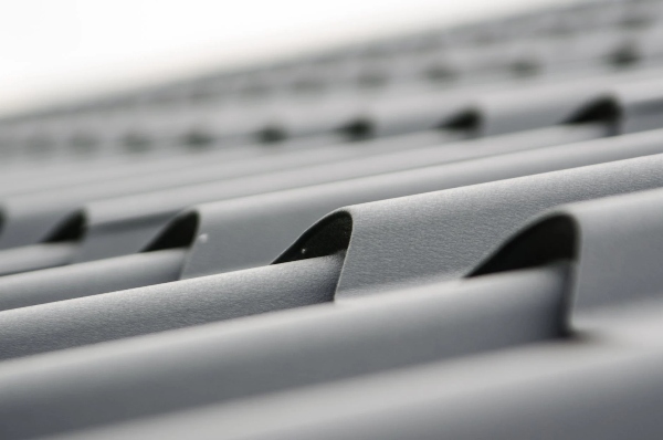 There is a close up shot of sheet metal roofing panels fit together on a homeowner's roof.